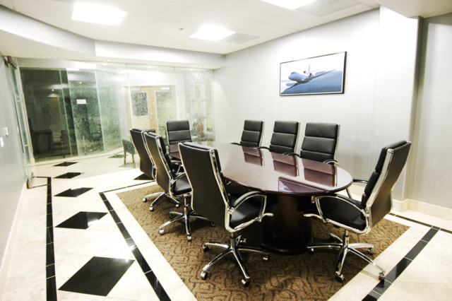 Conference room with 8 swivel chairs, a big table, glass door and travertine floors.